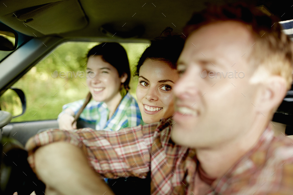 Three passengers in the cab of a pickup truck. One young man driving. Two young women sitting beside him.