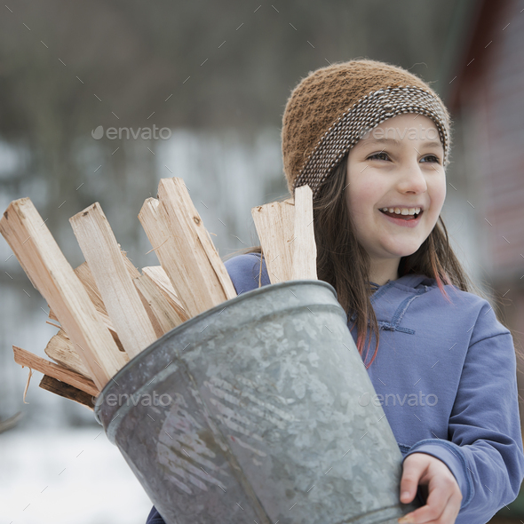 A girl carrying a bucket full of kindling and firewood. Stock Photo by