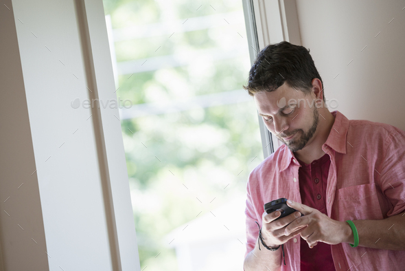 A man standing in a quiet corner of a cafe, using a smart phone.