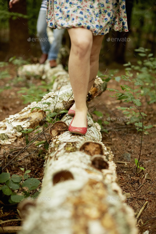 Two people walking along a fallen tree trunk in the woods.