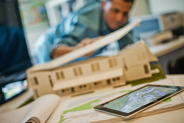 Architects working on a green construction project, using computer technology, in an office. An architect’s model of a house. Computer tablet.