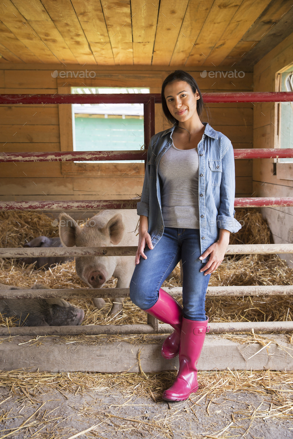 An organic farm in the Catskills. A woman beside a pig in a pen, standing in deep straw.