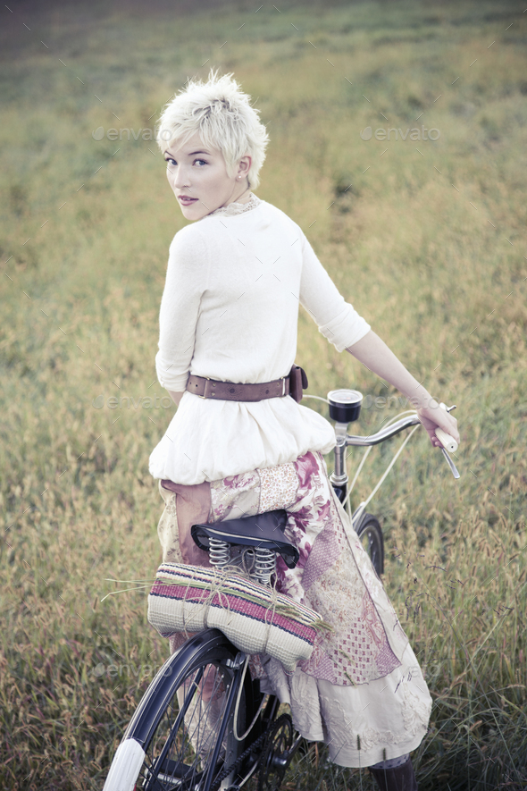 A girl in vintage clothing, paisley patterned cotton skirt with a bicycle in long grass.