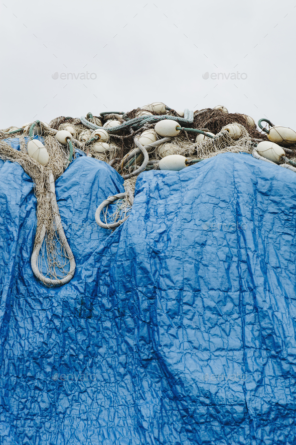 A blue tarpaulin covering stacked commercial fishing nets on a dockside