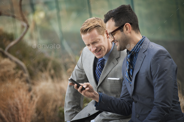 Two men standing side by side,looking at a cell phone screen or mobile phone.