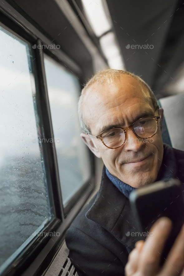 A mature man sitting by a window in a train carriage,using his ,mobile,keeping in touch on the move.