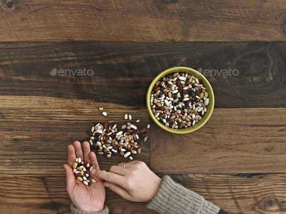 A person sorting different kinds of beans and pulses in her hands on a wooden table top.