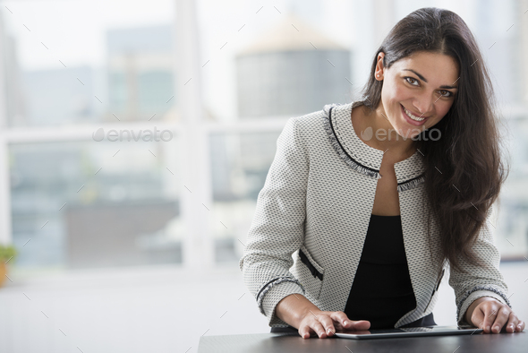 Young professionals at work. A woman at a work table using a digital tablet. Looking up and smiling.