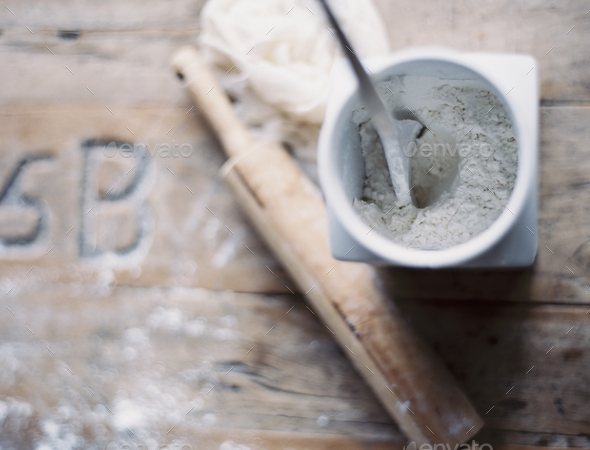 A rolling pin and jar of flour on a worn tabletop,View from above
