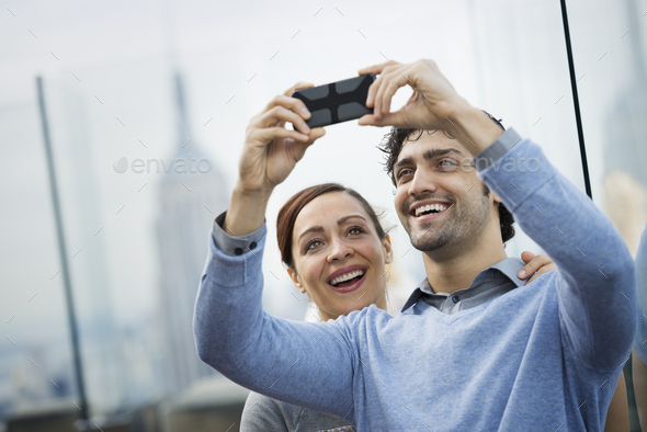 A young couple taking photographs with a mobile phone at a viewpoint over a city - Stock Photo - Images