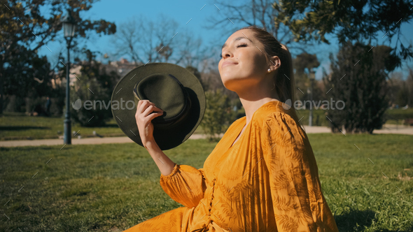 Young beautiful woman in bright orange overalls with hat dreamily resting on lawn in park - Stock Photo - Images