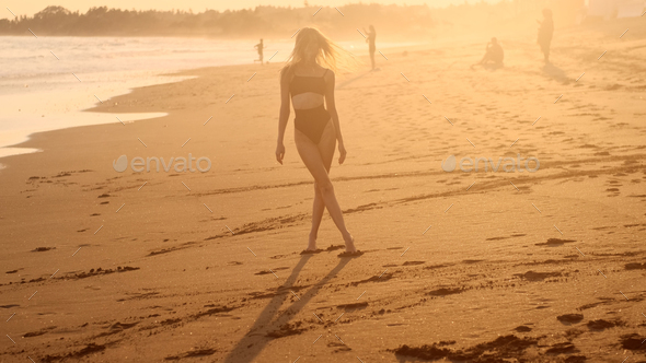 Beautiful slim girl in swimsuit meeting sunset by the ocean. Attractive model posing on beach