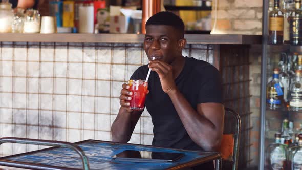 happy smiling black man drinks non-alcoholic fruit-based cocktail alt