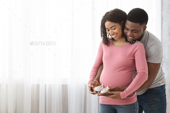 Cute black expecting family holding small baby shoes