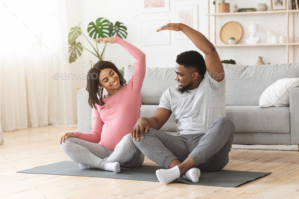 Active african expecting couple exercising together at home