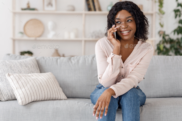 Happy black girl talking on mobile phone, relaxing on couch at home