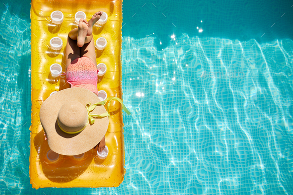 Top view little girl in hat relaxing in swimming pool, swims on inflatable yellow mattress - Stock Photo - Images