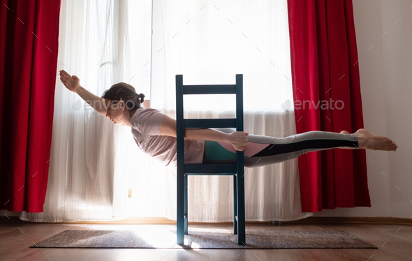 Young woman practicing yoga in Superman Pose or Viparita Shalabhasana using chair