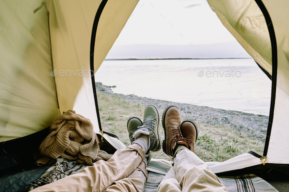Legs of young amorous couple in casualwear lying inside open tent by seaside