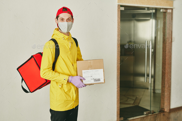 Happy young courier with big red backpack and cardboard packed box in hands - Stock Photo - Images