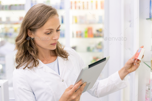 Young pharmacist with touchpad checking or looking for medicine in computer base