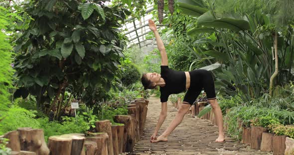 Young Woman is Doing Yoga Exercises in a Beautiful Botanical Garden Standing with Bare Feet on a