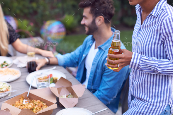 Close Up Of Woman Holding Bottle Of Beer With Friends In Garden At Home Enjoying Summer Garden Party