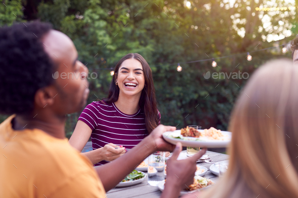 Friends In Garden At Home Sitting At Table Enjoying Food At Summer Garden Party