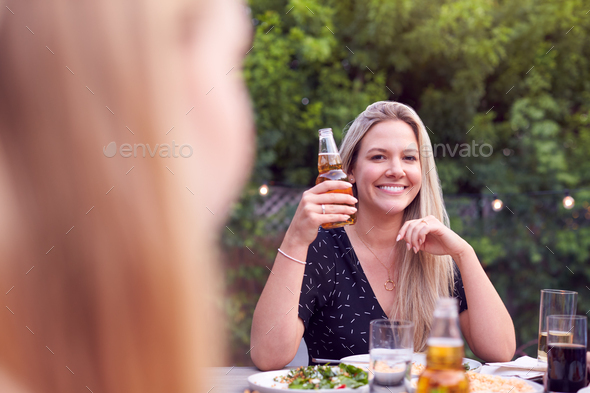 Woman Holding Bottle Of Beer With Friends In Garden At Home Enjoying Summer Garden Party