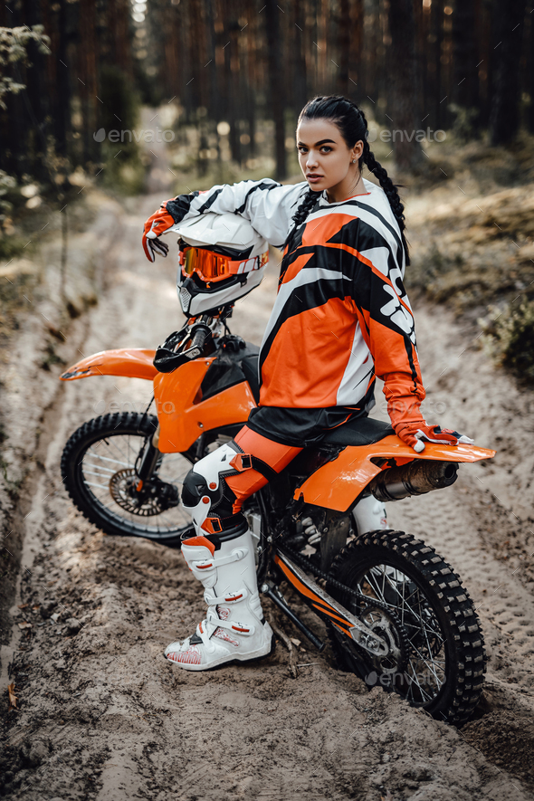 Beautiful young female racer riding motocross bike on a trail of sand in the woods