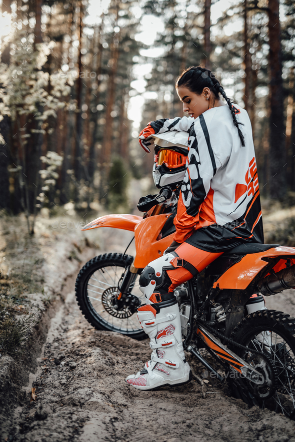 Beautiful young female racer riding motocross bike on a trail of sand in the woods