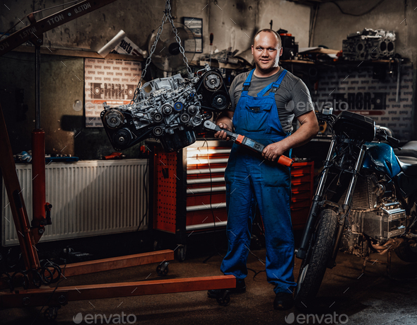 Professional mechanic stands next to the suspended flat engine and naked bike in garage - Stock Photo - Images