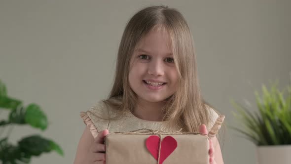 Cute Little Girl Smiling Giving Handmade Stylish Simple Gift Box in Craft Paper at Home with Small alt