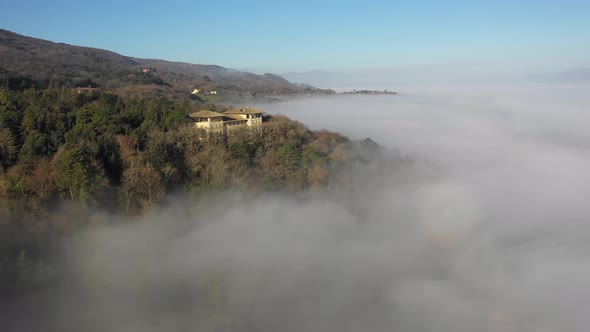 Aerial view of a palace with fog in the forest in Umbria, Italy alt