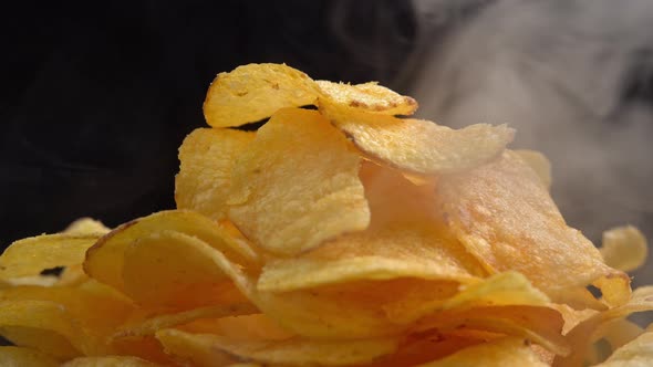 Craft crispy hot potato chips with smoke rotating on black background close up. Golden fried alt