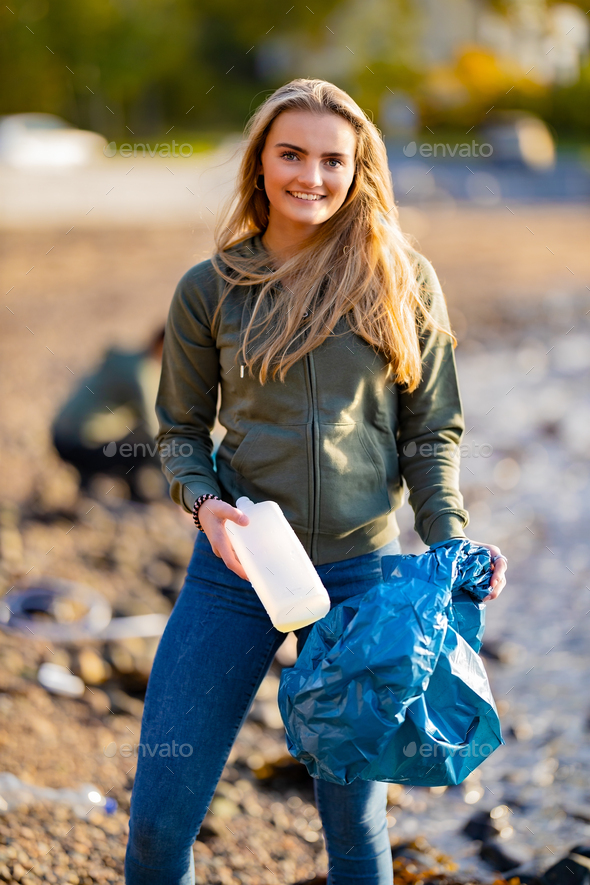 Smiling female volunteer holding bottle and garbage bag at beach - Stock Photo - Images