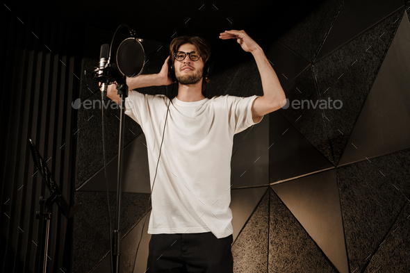 Young attractive male singer checking sound in headphones preparing record new song in sound studio