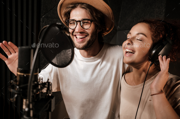 Portrait of young attractive man and woman happily singing together in sound recording studio