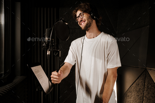 Attractive smiling singer in headphones happily recording song in professional sound studio
