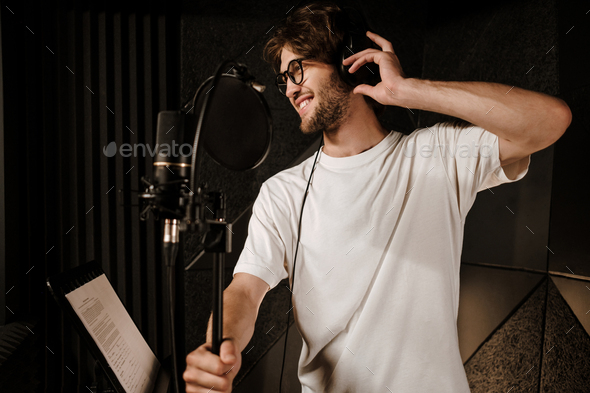 Young attractive male singer happily listening sound in headphones preparing record song in studio