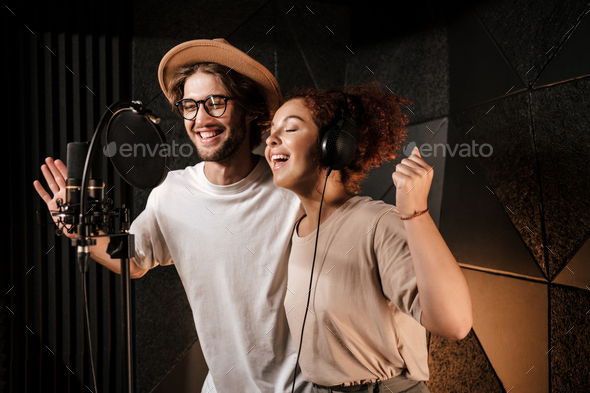 Young attractive musicians happily singing together recording new song in sound studio