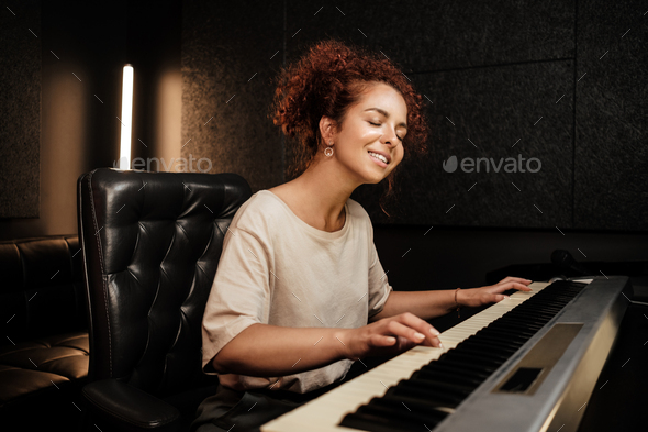Young pretty woman sensually playing on electric piano and singing a song in sound recording studio
