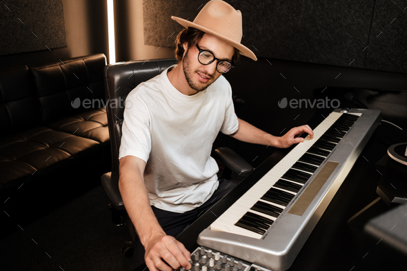 Young stylish musician composing new song on midi piano in sound recording studio