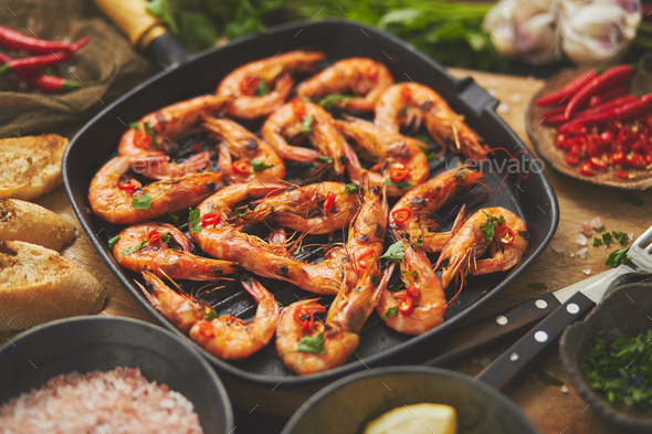 Tasty appetizing roasted shrimps prawns with spices on pan with ingredients on rusty background - Stock Photo - Images