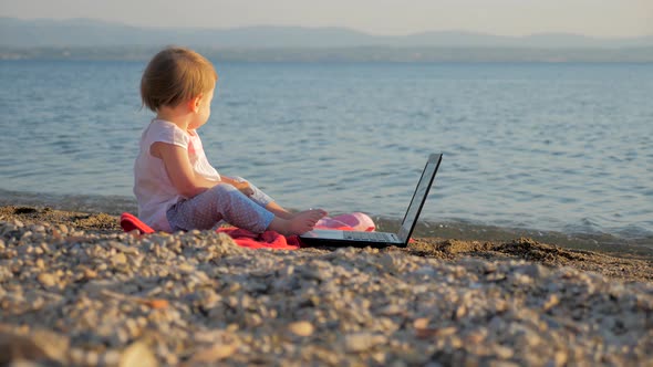 Toddler Sitting with Notebook on Seashore. New Generation of People Who Combine Work and Vacation