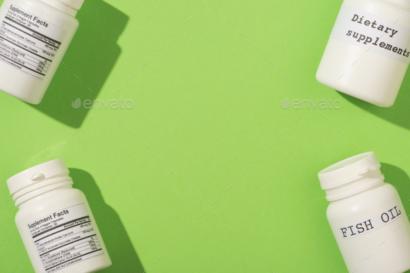 Top View of Containers With Fish Oil And Dietary Supplements Lettering on Green Background