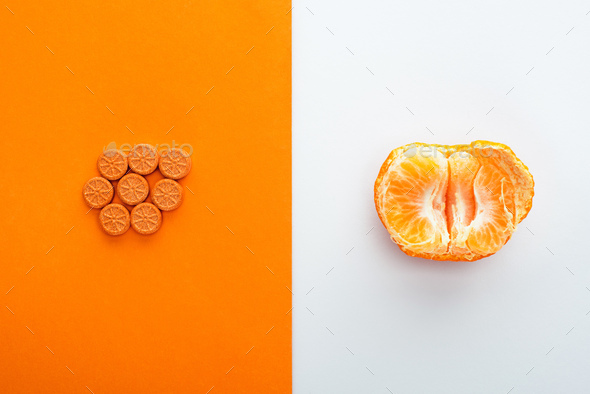 Top View of Pills And Mandarin Half on White And Orange Background