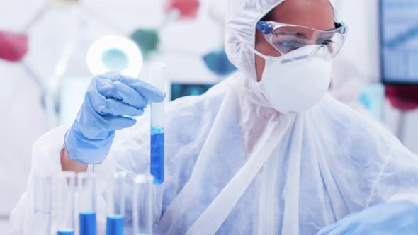 Female Researcher in Coverall Equipment Holding a Test Tube with Smoking Blue Solution alt