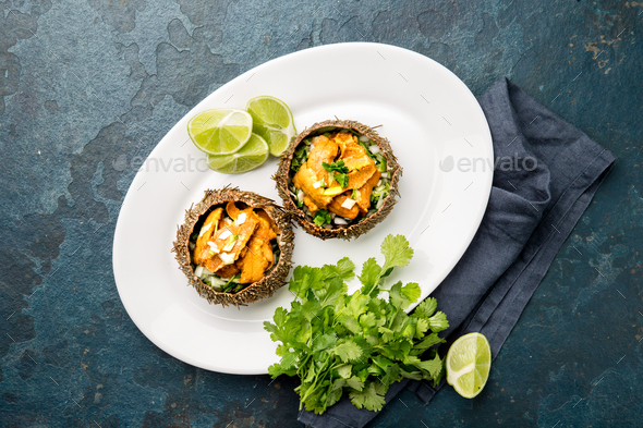 Fresh opened sea urchins. Caviar of sea urchins with onion, cilantro and lemon inside of shell of - Stock Photo - Images