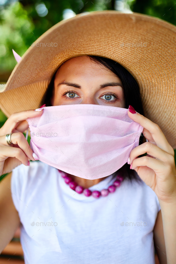 Portrait of woman in straw hat takes off pink protective mask